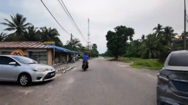 Batu Pahat, Johor, Malaysia - May 31 2024: Slow dolly move along a quiet countryside road lined with green trees and open skies.
