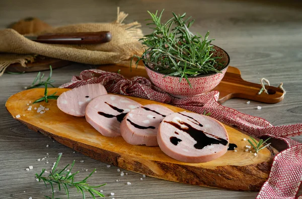 slices of Bologna IGP mortadella on a rustic wooden cutting board with a balsamic vinegar glaze from Modena