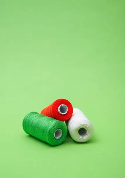 Various spools of sewing cotton thread of different colors italian flag on green background