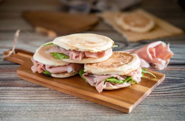 Close-up of delicious stack of crescentine tigelle with mortadella and rocket on a wooden board, ready to be enjoyed clipart