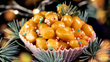 Renkli süslemelerle süslenmiş Napoli struffoli hamur toplarının altı resmi ve arka planda bokeh ışıkları olan bir tutam çam ağacı.