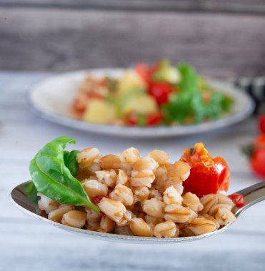 Domates ve fesleğenle tatlandırılmış Farro salatası kaşıkta sunuluyor, sağlıklı ve lezzetli mutfağın vücut bulmuş hali.