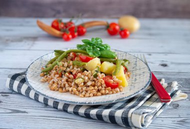 Patatesli, yeşil fasulyeli, kiraz domatesli, kabaklı ve fesleğen yapraklı Farro salatasının yakın çekimi.