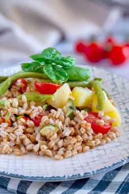 Patatesli, yeşil fasulyeli, kiraz domatesli, kabaklı ve fesleğen yapraklı Farro salatasının yakın çekimi.