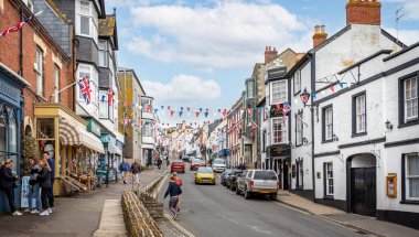 Broad Caddesi 'ne bakıyorum, 7 Mayıs 2023' te Lyme Regis, Dorset, İngiltere 'de renkli kiraz kuşları ve Union Jack bayraklarıyla süslenmiş.