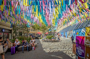 16 Ağustos 2023 'te İngiltere' nin Avon, Bath kentindeki Southgate Alışveriş Merkezi 'nde parlak renkli kurdeleler altında noktalı ışıkta oturan müşteriler