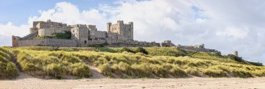 Bamburgh Kalesi 'nin panoramik kıyı manzarası 25 Eylül 2023' te Bamburgh, Northumberland, İngiltere 'deki kum tepelerinden yükseliyor.