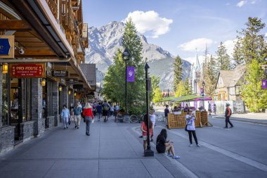 Banff Bulvarı 'nda 8 Haziran 2023' te Banff, Alberta, Kanada 'da Cascade Dağı' nın arka planında alışveriş ve yayalar var.