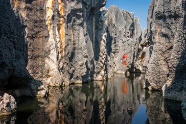 Dramatic Karst limestone geologic formations rising from lake in Stone Forest National Geo-park, Yunnan, China clipart