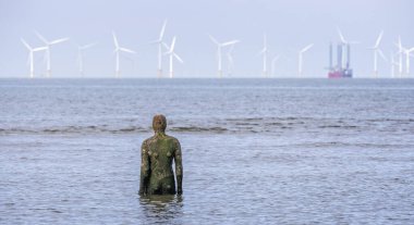 Antony Gormley iron man installation looking out to sea at offshore wind farm at Crosby Beach, near Liverpool, Lancashire, UK on 21 May 2024 clipart