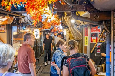 23 Eylül 2023 'te Shinjuku, Tokyo, Japonya' da Omoide Yokocho 'nun dar sokaklarında küçük restoranların önünden geçen turistler