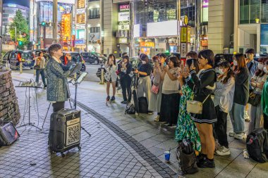 Japon sokak müzisyeni, 23 Eylül 2023 'te Shinjuku, Tokyo, Japonya' da genç bayanlara şarkı söylüyor.