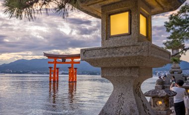 Iconic turuncu Torii kapısı, 29 Eylül 2024 'te Japonya' nın Miyajima Adası 'nda gün batımında Itsukashima türbesi yakınlarında büyük bir taş fenerle birlikte yüzüyor.