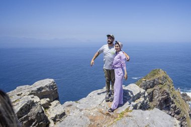 Couple standing precariously on cliff top edge for photo at cape Point, near cape Town, South Africa on 7 December 2024 clipart