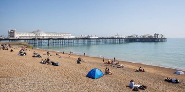 Brighton Palace Rıhtımı ve plajı 27 Nisan 2025 'te Brighton, Sussex, İngiltere plajında güneşlenenlerle dolu.