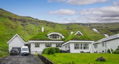 Faroe Adaları 'nın arka planında 3 Haziran 2025' te Fornavegur, Lamba 'da şelaleleri ve uçurumları olan çim çatılı modern ev.