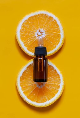 Cam şişedeki turuncu organik aromatik yağ ve taze portakal dilimlerinden oluşan bir pipet.