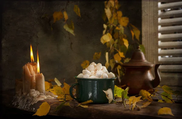 Cozy autumn still life with a cup of cocoa with marshmallow and cinnamon, burning candles and autumn leaves