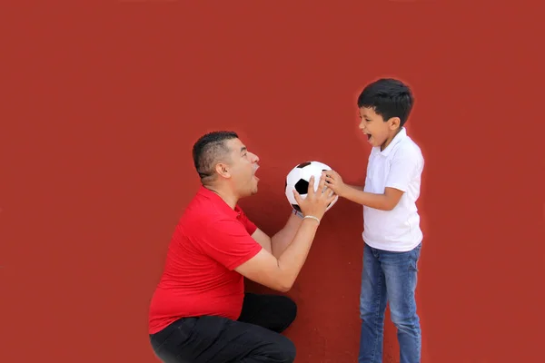 Latino dad and son share their love for soccer, they take a ball with their hands excited to watch the World Cup football game