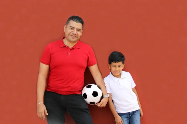 Latino dad and son share their love for soccer, they take a ball with their hands excited to watch the World Cup football game