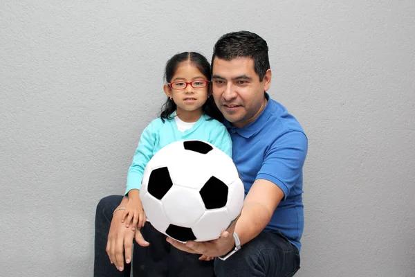 Latino dad and daughter share their love for soccer, they take a ball with their hands excited to watch the World Cup football game