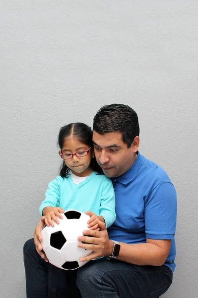Latino dad and daughter share their love for soccer, they take a ball with their hands excited to watch the World Cup football game