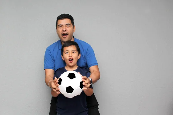 Hispanic dad and son share their love for soccer, they take a ball with their hands excited to watch the football game