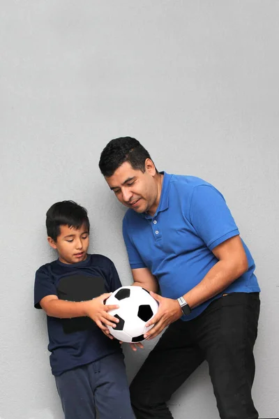 Hispanic dad and son share their love for soccer, they take a ball with their hands excited to watch the football game