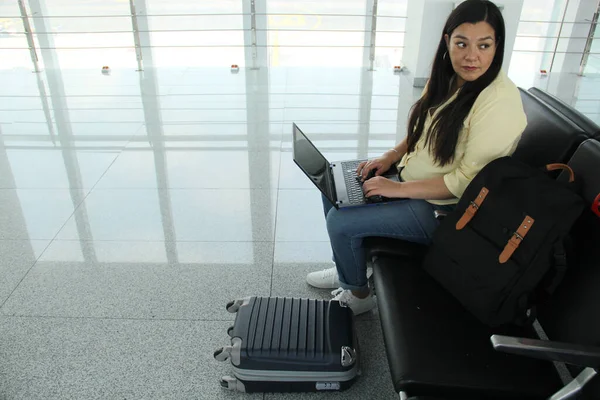 stock image Latin adult woman works with her laptop next to her luggage in the airport waiting room while waiting for her flight, she looks stressed, distressed, tense suffering from burnout before her trip