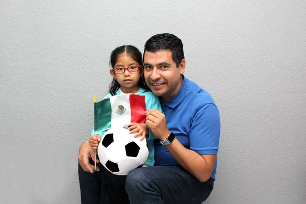 Mexican dad and daughter share their love for soccer, they take a ball and flag with their hands excited to watch the  football game