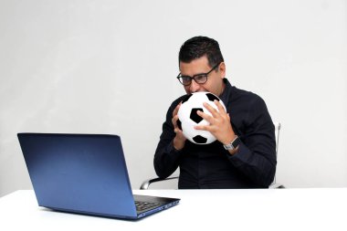 Latin yetişkin ofis çalışanı, iş saatleri boyunca futbol maçlarını bilgisayarından izliyor. Onu futbol topunun yanında sinirli, üzgün, stresli ve sinirli görüyor.