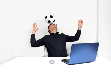 Latin yetişkin ofis çalışanı, iş saatleri boyunca futbol maçlarını bilgisayarından izliyor. Onu futbol topunun yanında heyecanlı, gergin ve şaşırmış görüyor.