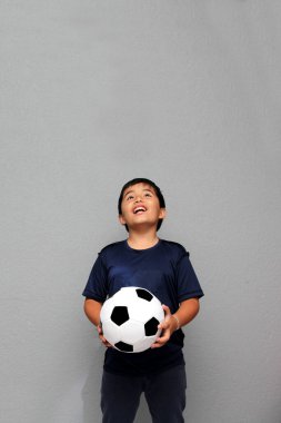Latin kökenli 8 yaşındaki çocuk futbol topuyla oynuyor. Futbol maçını izleyeceği için çok heyecanlı ve takımının kazandığını görmek istiyor.