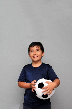 Latin kökenli 8 yaşındaki çocuk futbol topuyla oynuyor. Futbol maçını izleyeceği için çok heyecanlı ve takımının kazandığını görmek istiyor.