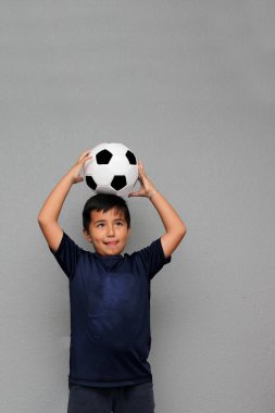 Latin kökenli 8 yaşındaki çocuk futbol topuyla oynuyor. Futbol maçını izleyeceği için çok heyecanlı ve takımının kazandığını görmek istiyor.