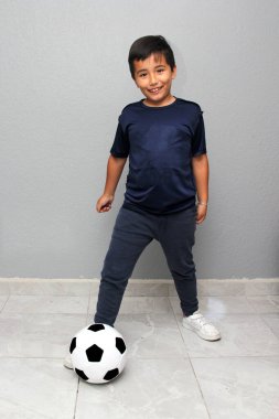 Latin kökenli 8 yaşındaki çocuk futbol topuyla oynuyor. Futbol maçını izleyeceği için çok heyecanlı ve takımının kazandığını görmek istiyor.