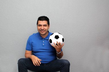 Latin yetişkin bir adam futbol topuyla oynuyor. Maçı izleyeceği için çok heyecanlı ve takımının kazandığını görmek istiyor.