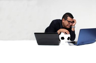 Latin yetişkin ofis çalışanı, iş saatleri boyunca dizüstü bilgisayarından futbol maçlarını izliyor. Onu futbol topunun yanında sinirli, üzgün, stresli ve sinirli görüyor.