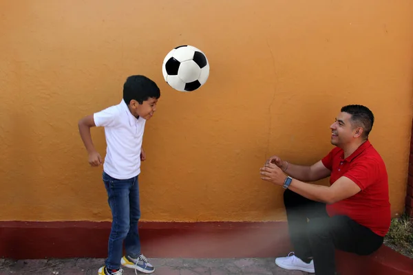 Latino dad and son share their love for soccer, they take a ball with their hands excited to watch the football game