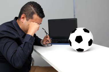 Latin yetişkin ofis çalışanı, iş saatleri boyunca dizüstü bilgisayarından futbol maçlarını izliyor. Onu futbol topunun yanında sinirli, üzgün, stresli ve sinirli görüyor.