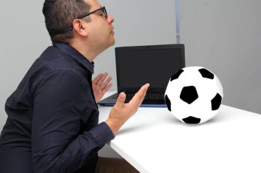 Latin yetişkin ofis çalışanı, iş saatleri boyunca dizüstü bilgisayarından futbol maçlarını izliyor. Onu futbol topunun yanında sinirli, üzgün, stresli ve sinirli görüyor.