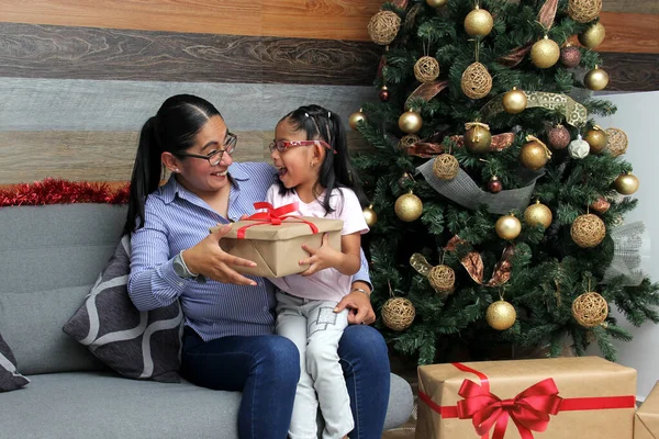 Divorced single mom and daughter Latina brunettes with glasses have Christmas presents sitting by the tree with spheres give each other hugs and kisses show their love in solitude