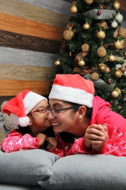 Bekar anne ve kızı, pijama giymiş gözlüklü Latin esmerler Noel ağacının yanında Noel Baba şapkasıyla oynuyorlar. Birbirlerine sarılıyorlar ve öpüşüyorlar.
