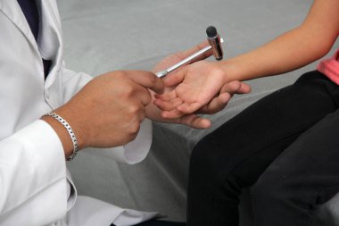 Latino doctor medic and girl patient in medical office checks her reflexes on hammer in her checkup to find disease diagnosis
