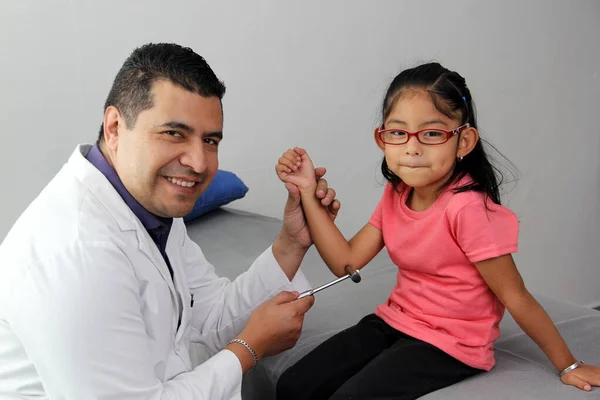Latino doctor medic and girl patient in medical office checks her reflexes on hammer in her checkup to find disease diagnosis