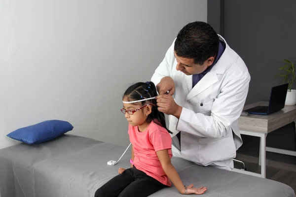Latino pediatrician specialist doctor measures the head of his patient, a small 4-year-old brunette girl checks her measurements during a medical check-up in the office