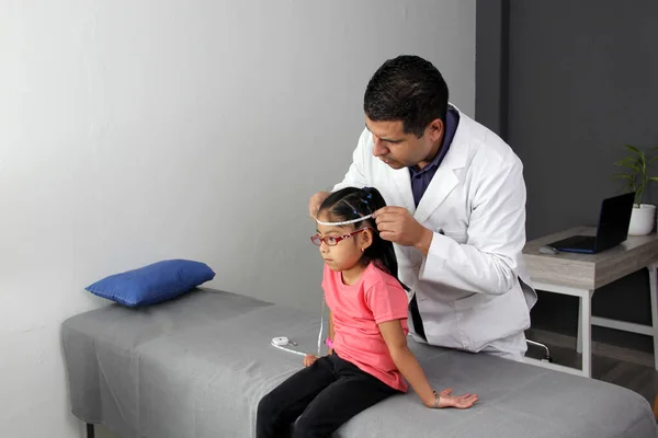 Latino pediatrician specialist doctor measures the head of his patient, a small 4-year-old brunette girl checks her measurements during a medical check-up in the office