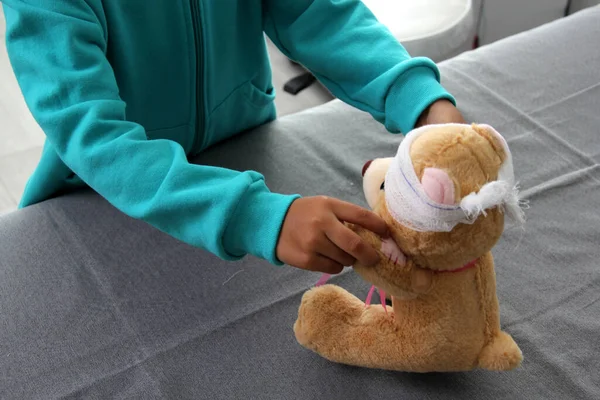 4-year-old brunette Latina girl with glasses represents mistreatment and physical abuse in her teddy bear with bandages on her head, she cares for him and heals his wounds