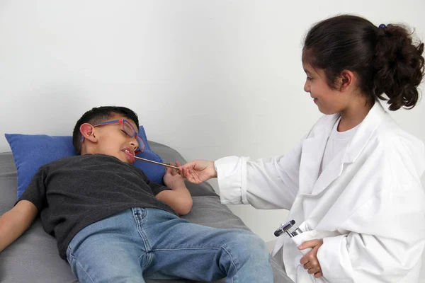 Latino girl and boy play to be a doctor with a white coat that is too big for her and patient who acts to feel sick very entertaining and funny they make jokes