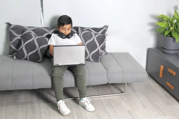 9-year-old Hispanic boy plays video games on his laptop with headphones leading to being overweight and poor sitting posture
